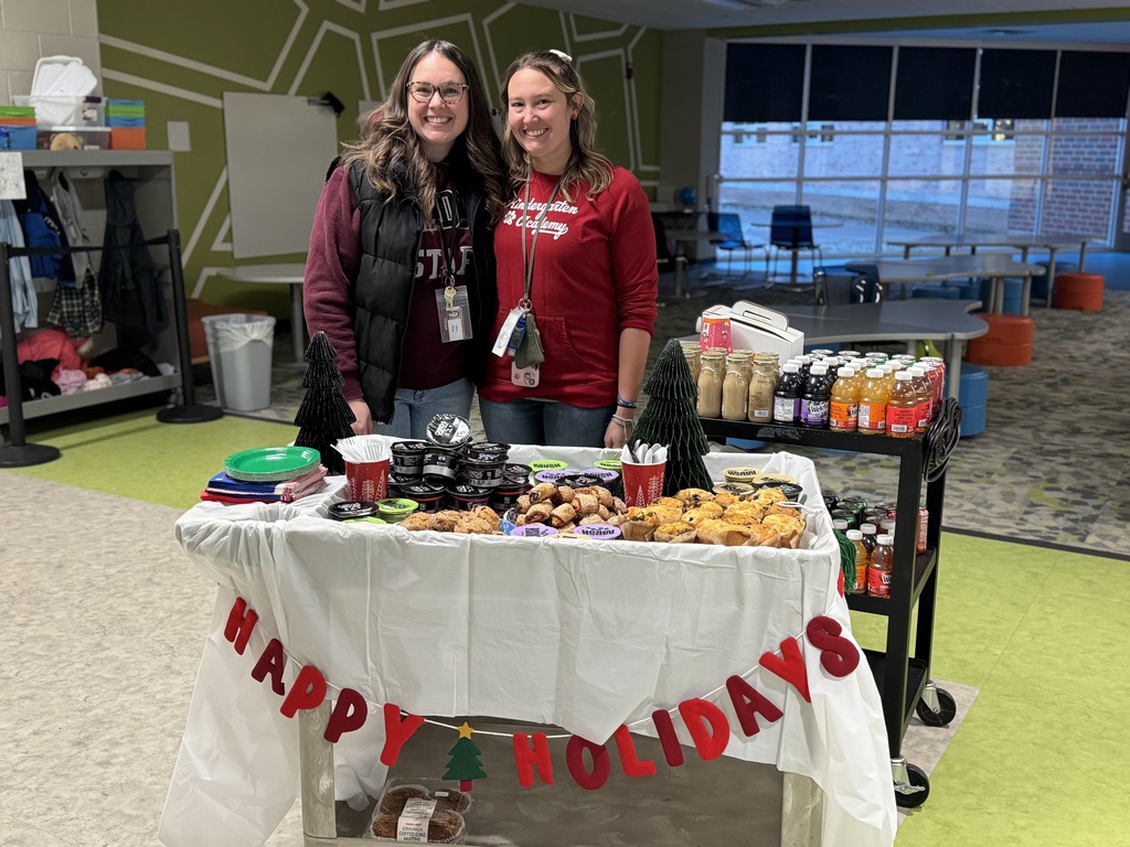 Two adults standing behind a holiday cheer cart full of snacks.