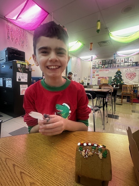 A student proudly shows off his handmade gingerbread house.