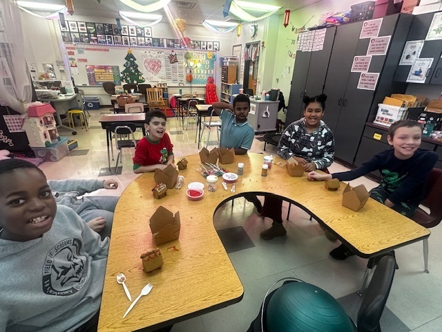 Students at a table behind their handmade gingerbread houses.