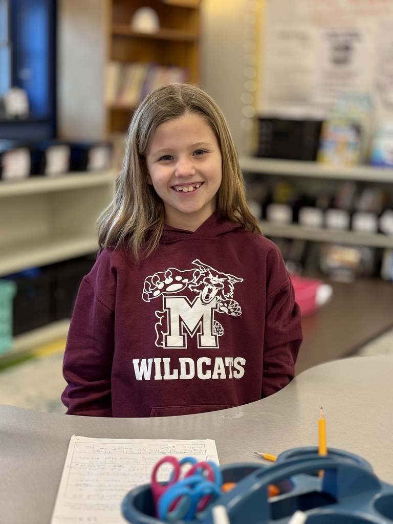 A student smiling at a desk while wearing a maroon sweatshirt.