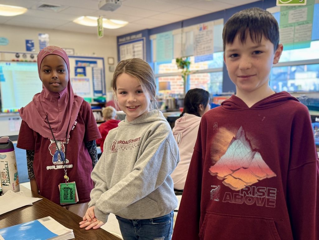 Three students proudly wearing maroon and gray shirts while standing in their classroom.