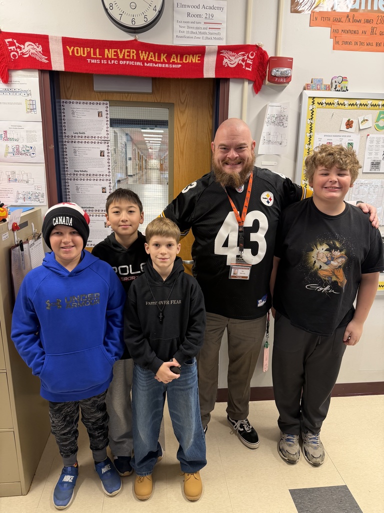 A principal wearing a Steelers jersey poses for a photo with a small group of students.