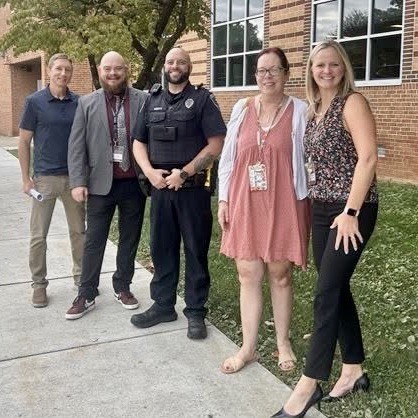 A police officer stands with a group of educators in front of a school