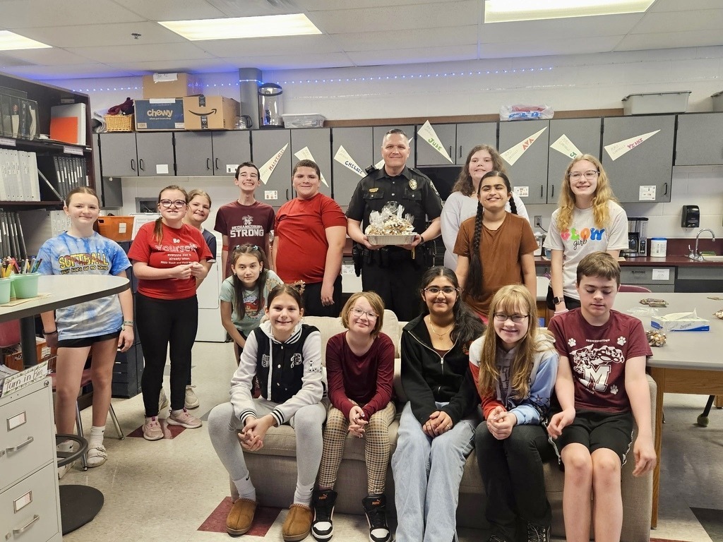 A police officers stands with a group of students who presented him with a gift.