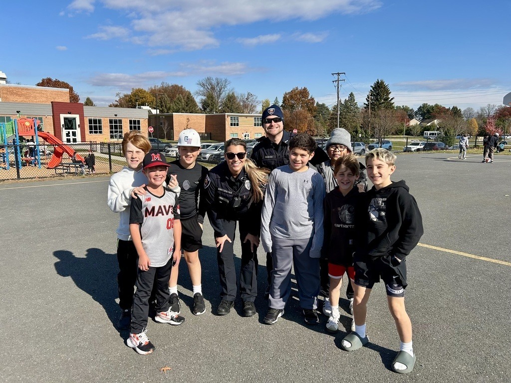 Police officers playing kickball on a playground with a group of students.