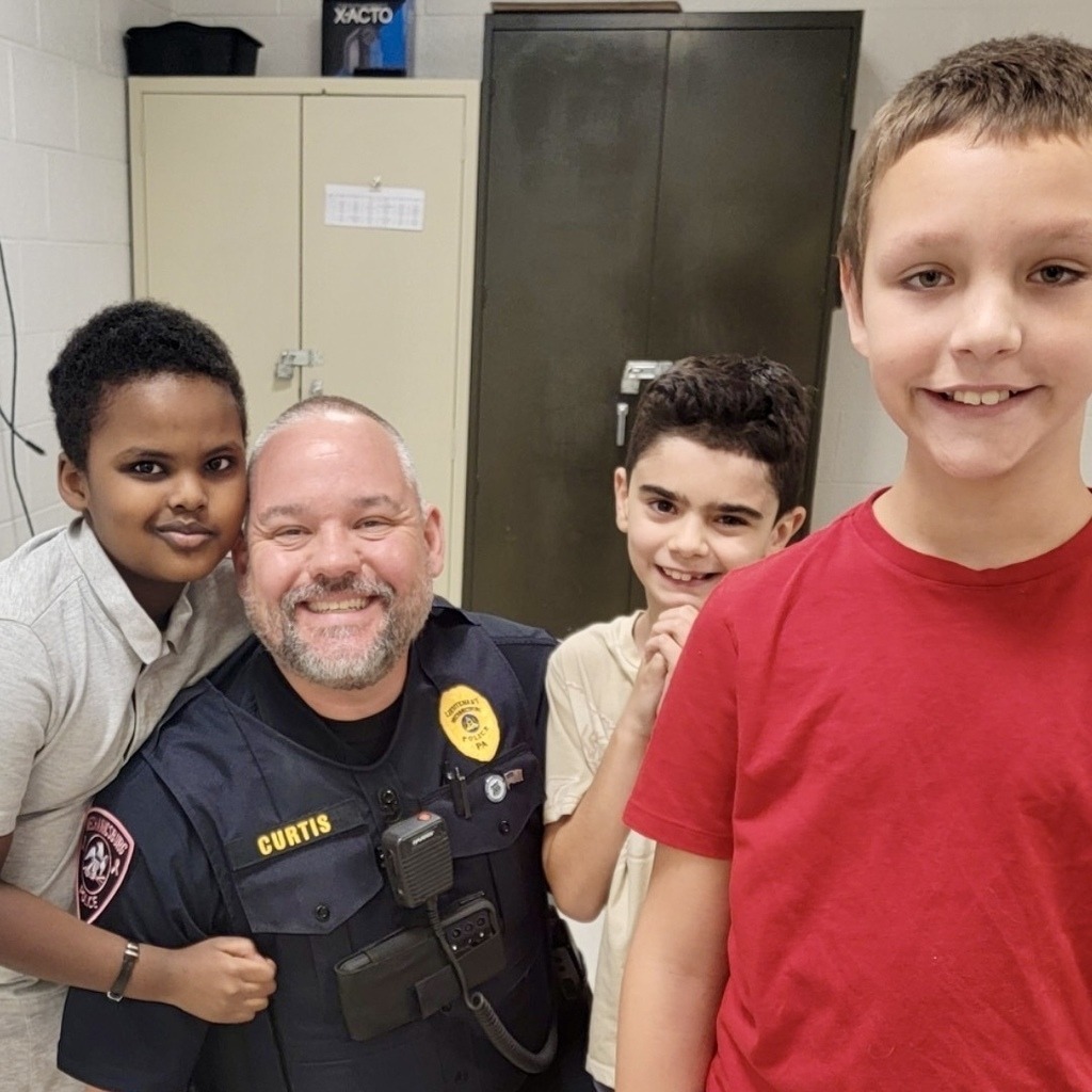 A police officer happily poses for a picture with some students.