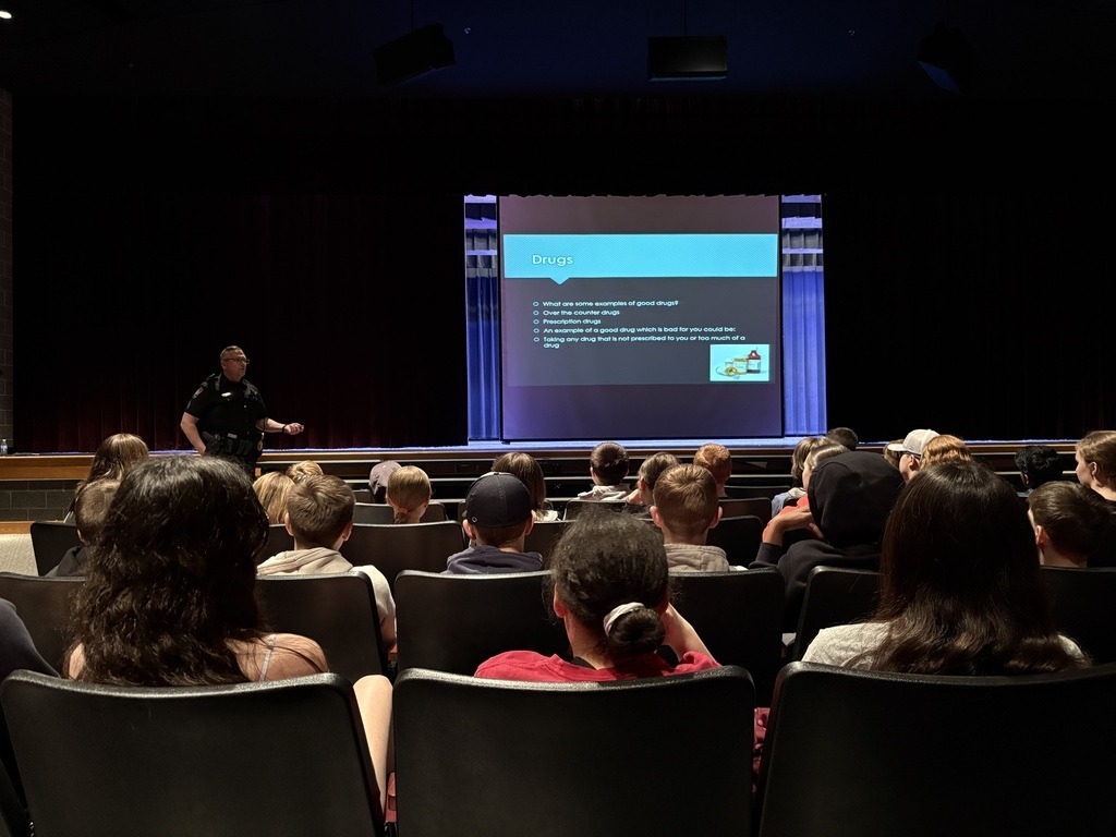 A police officer gives a presentation to a group of students in an auditorium.