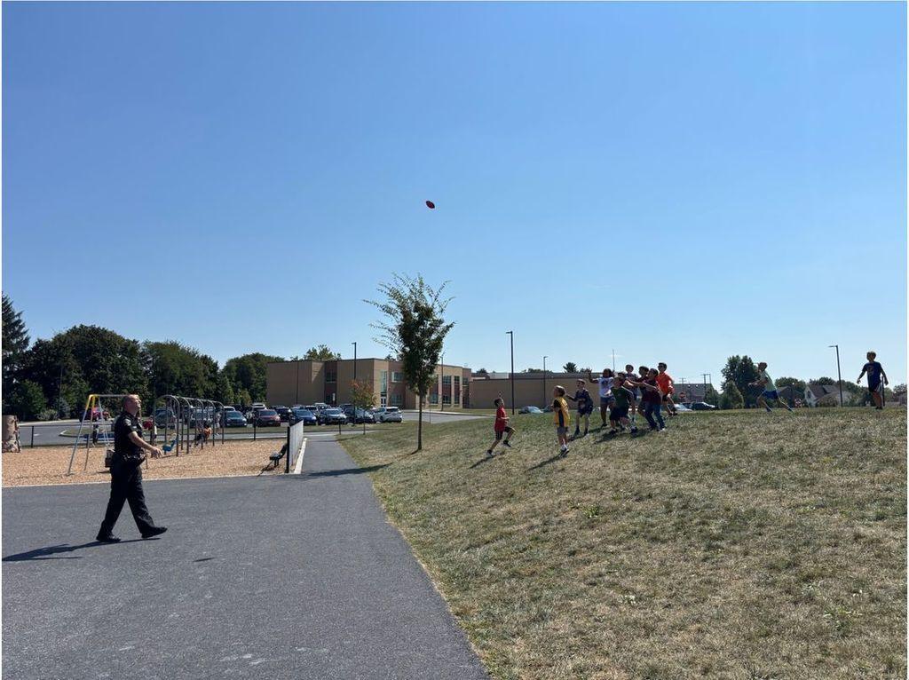 A police officer plays catch with a group of young students on a school playground.