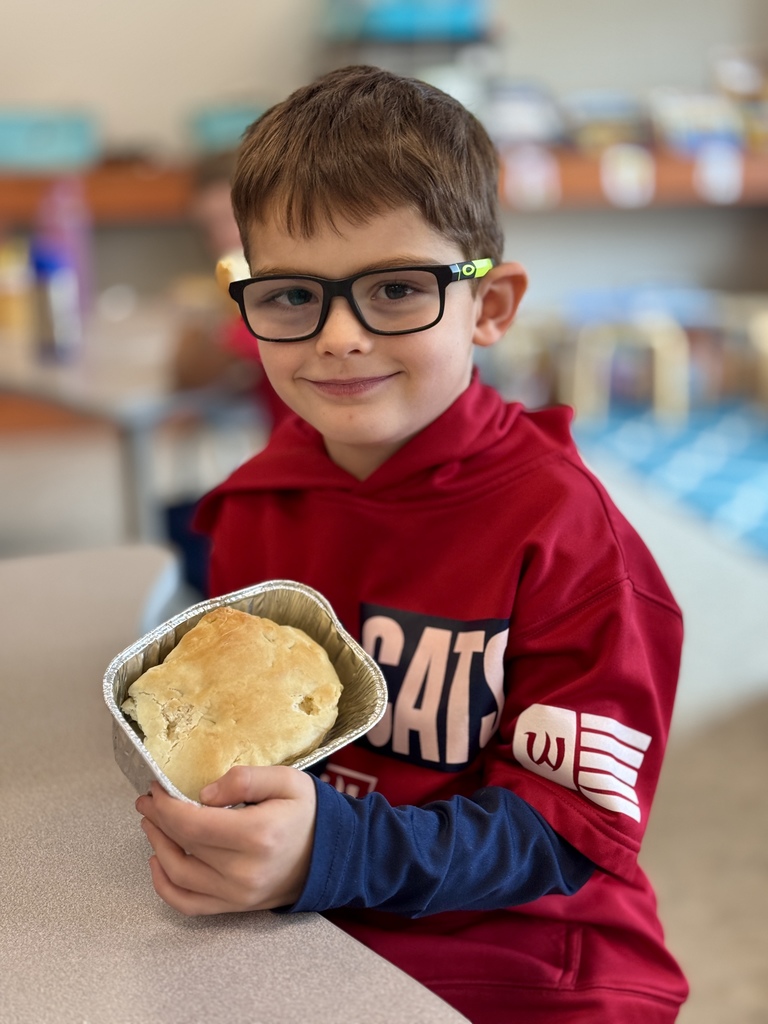 A young boy proudly holds up a loaf of homemade bread.