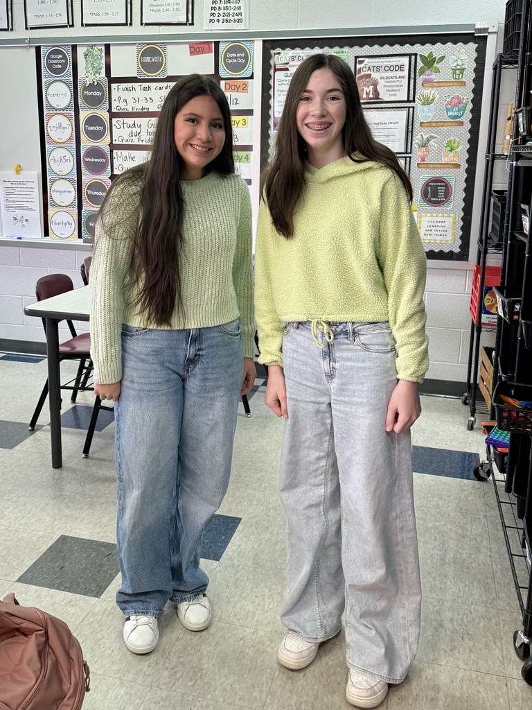 Two students standing side by side in nearly matching sweaters, jeans, and sneakers.
