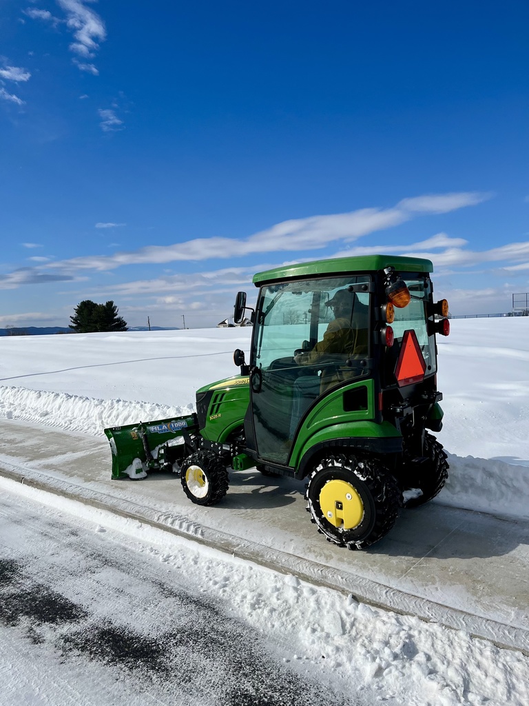 Maintenance crews clear sidewalks in a green tractor.