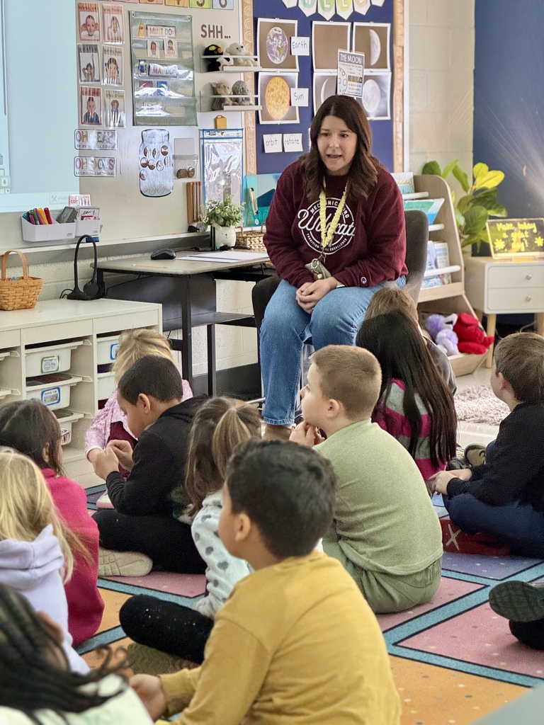 A teacher sitting on a chair talking to students about math.