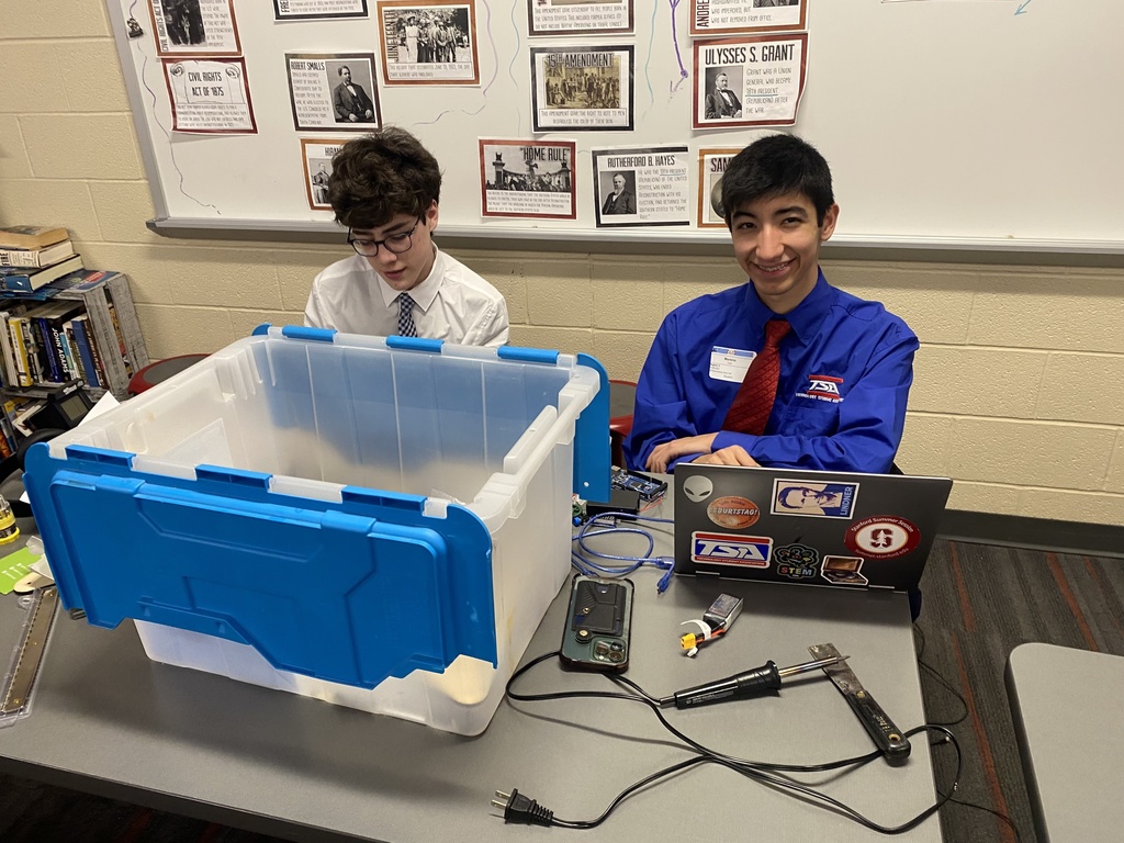 Students behind a table full of electronics as part of a TSA competition.
