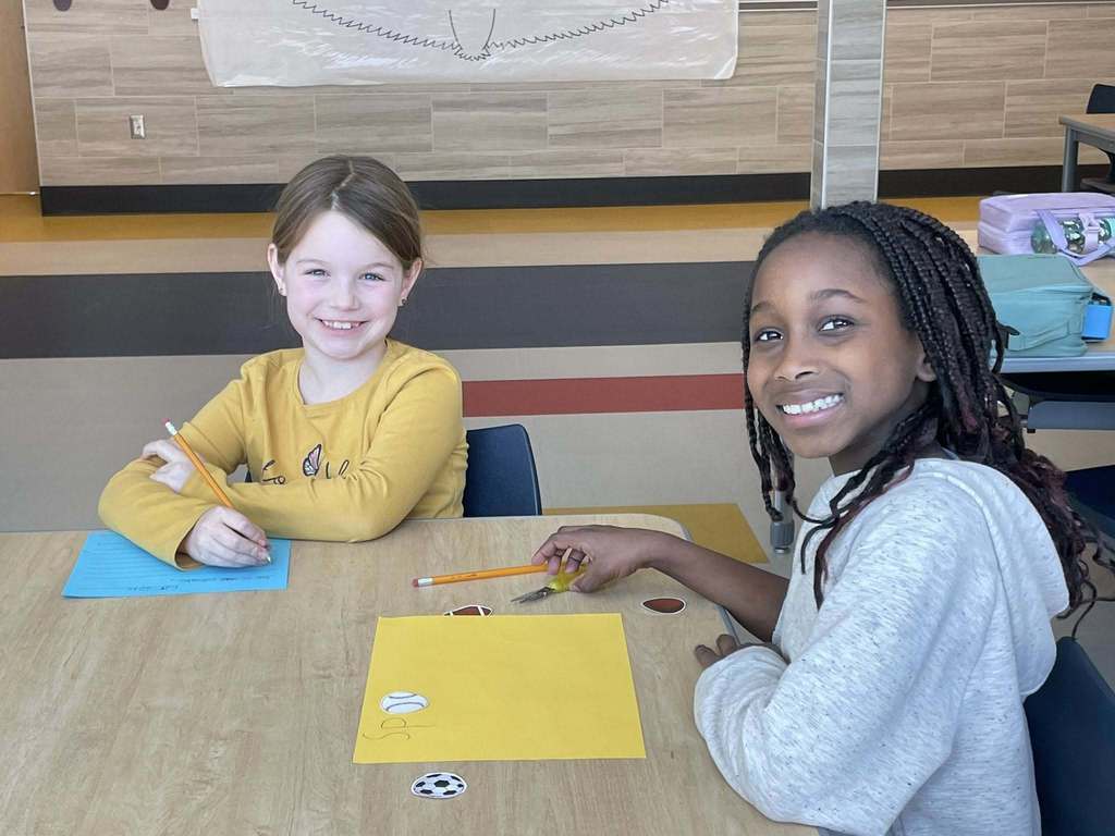 Two young students work together at a table to make signs.