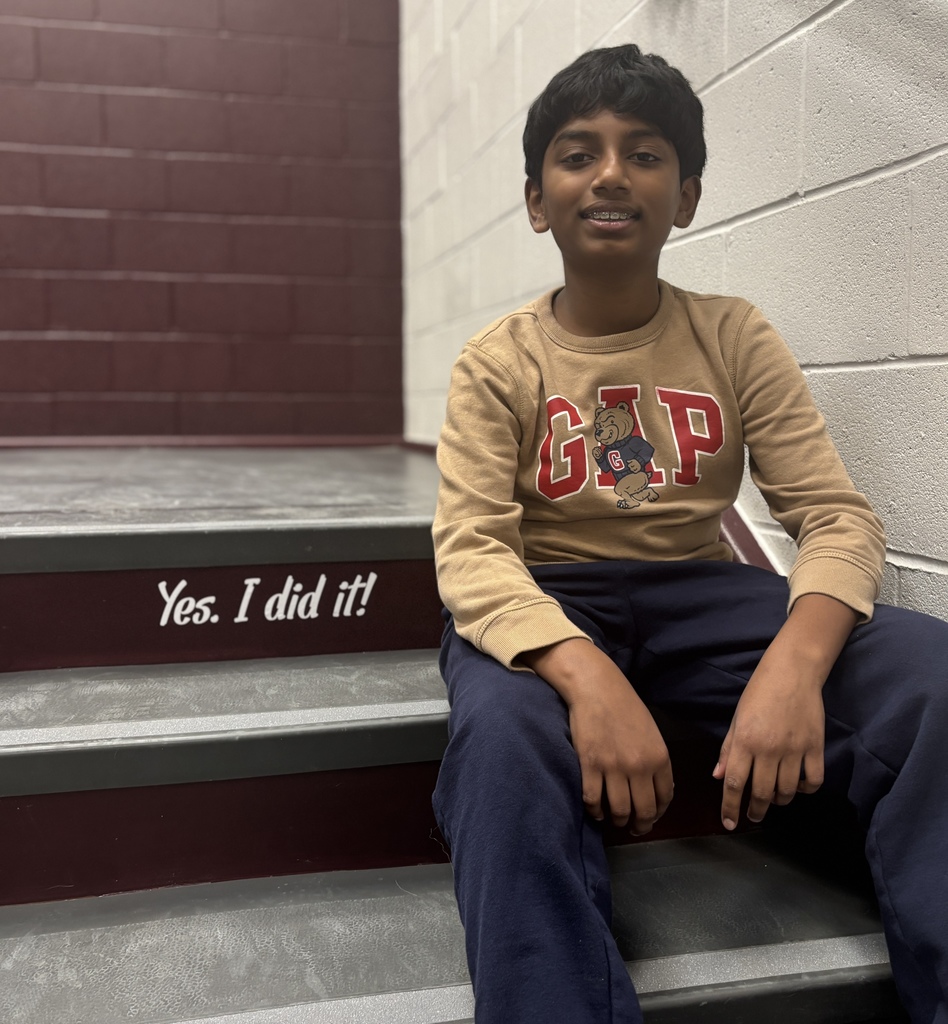 A young student sitting on a step in front of a sign that says Yes. I did it!
