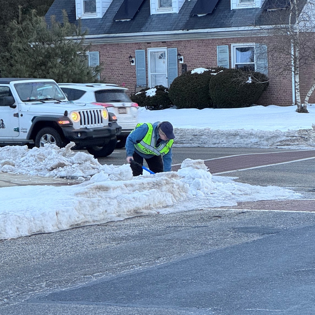 Crossing guard shovels snow and ice from a crosswalk.
