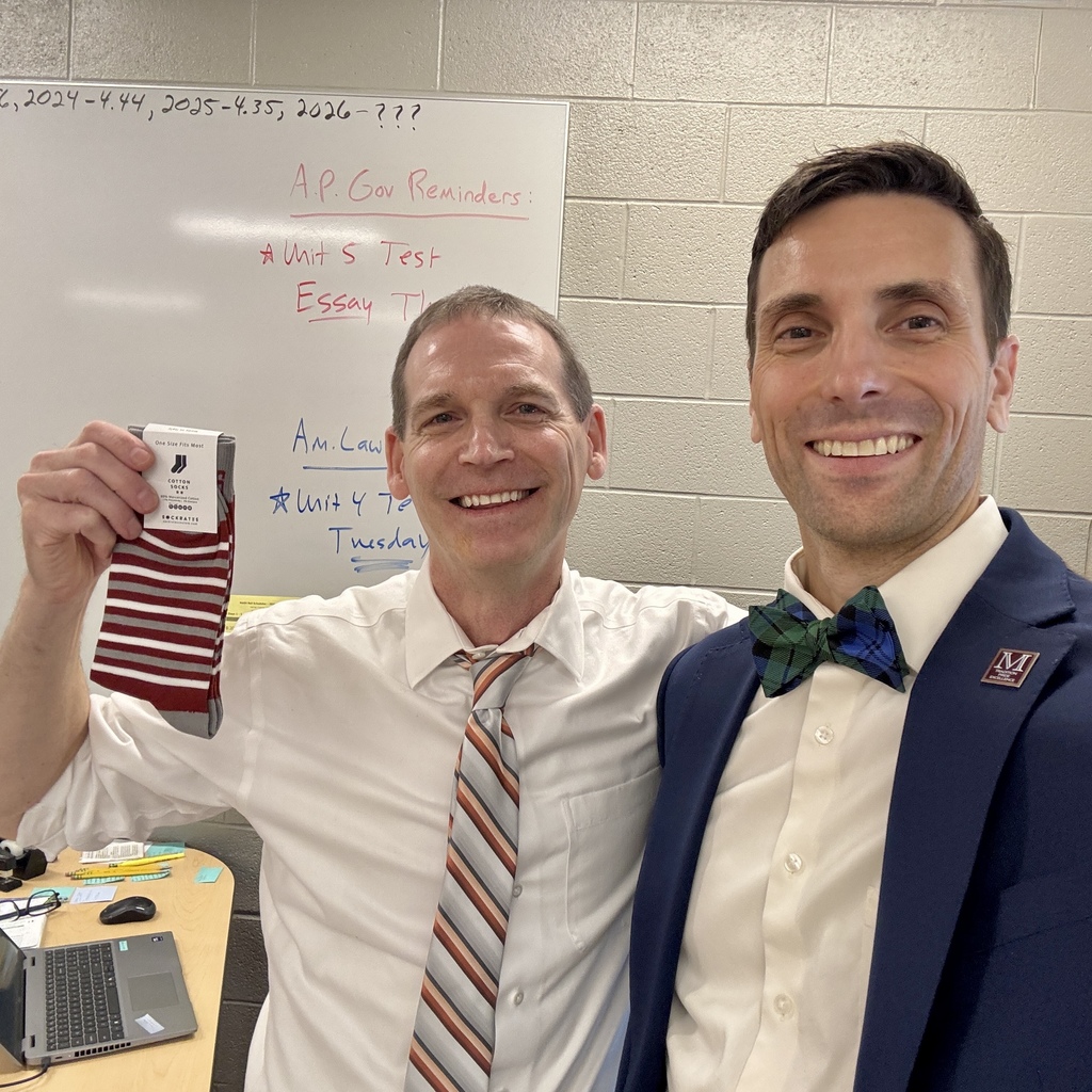 Two men standing side by side while one holds a pair of stripped socks.
