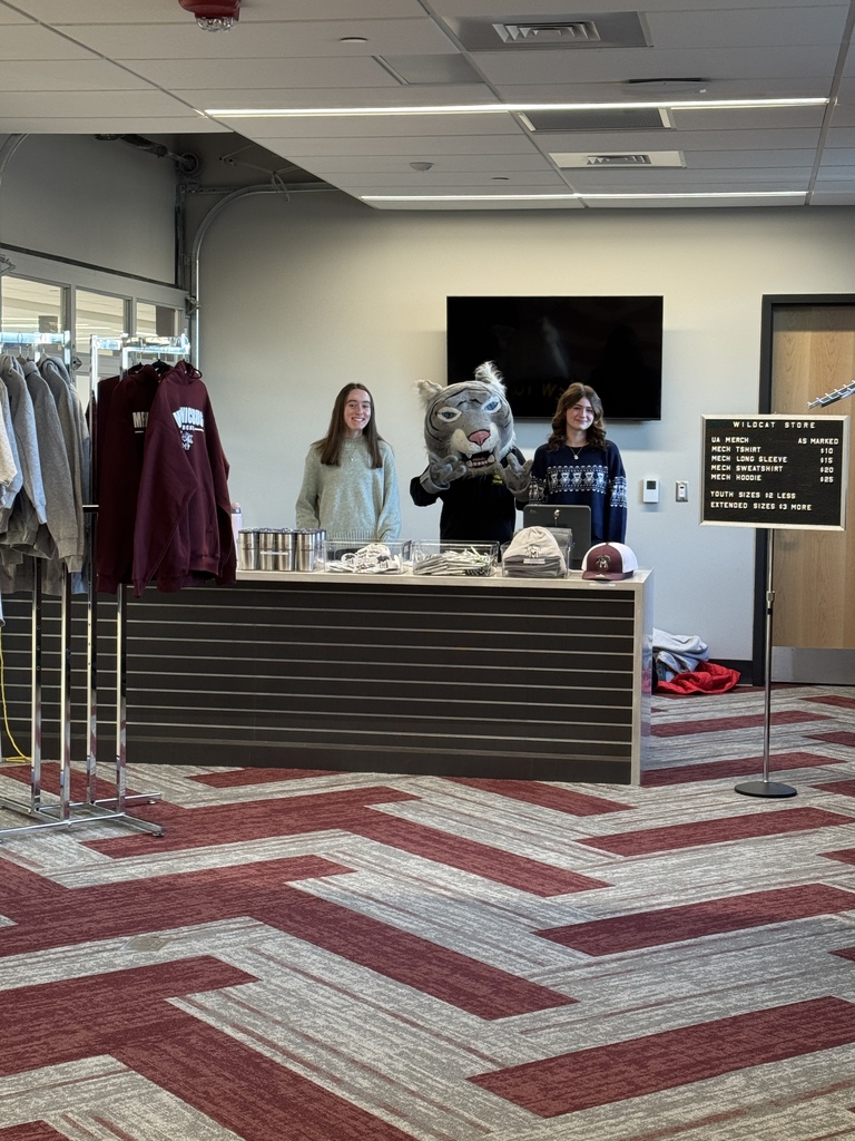 Students and our mascot pose behind the counter of a new student store.