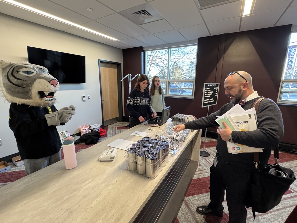 A staff member shops at the new school store while a mascot helps ring up the purchase.