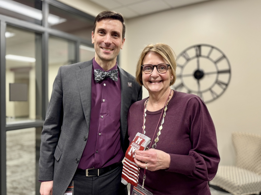 Two adults standing next to each other and one is holding a pair of maroon branded socks.