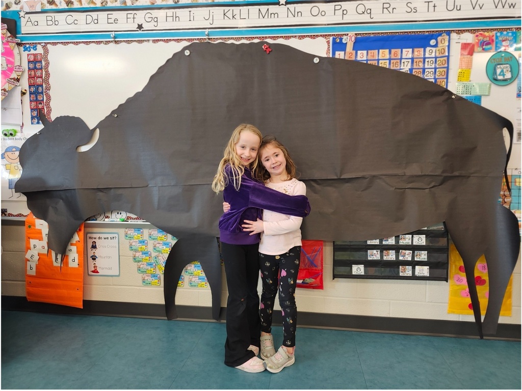 Two young students stand in front of a life size silhouette of a Bison.