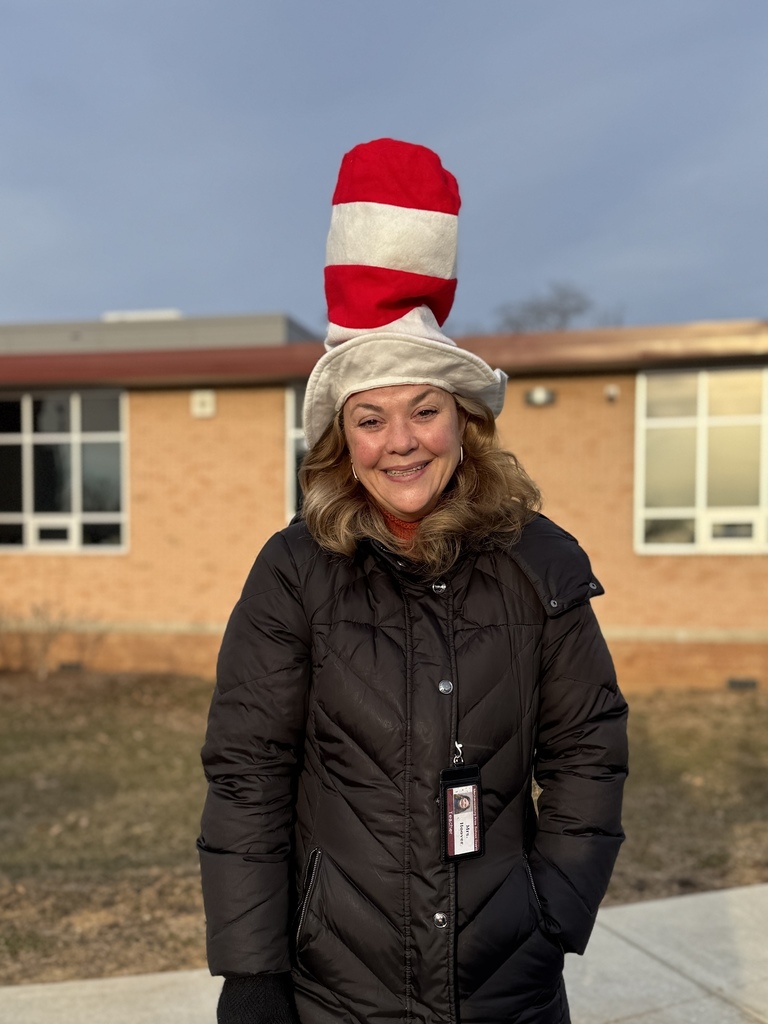 A reading teacher standing outside a school in a red and white striped Dr. Seuss hat.
