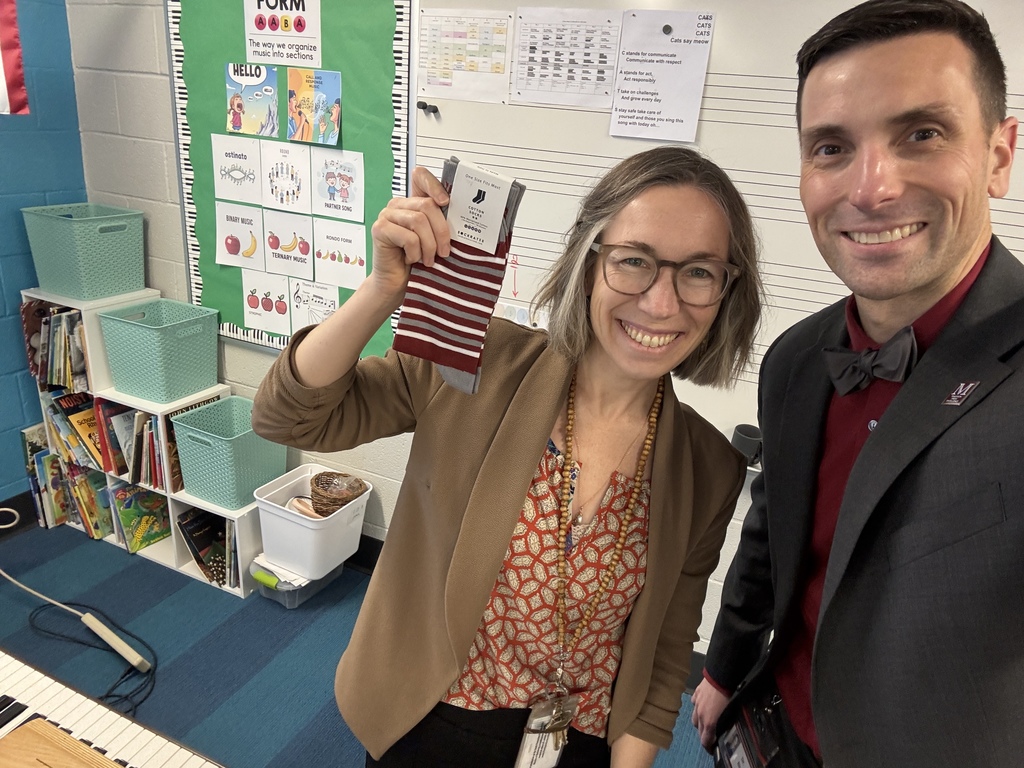 A teacher holds a pair of branded socks while standing next to a man in a suit.