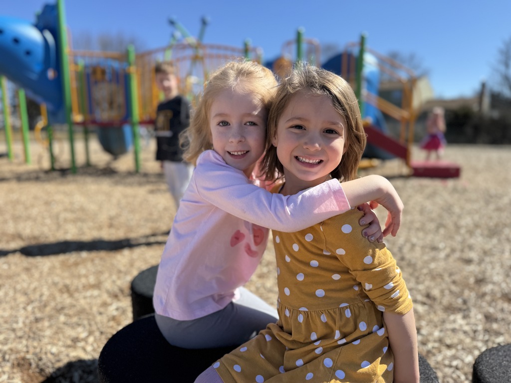 Two young friends hugging on a school playground.