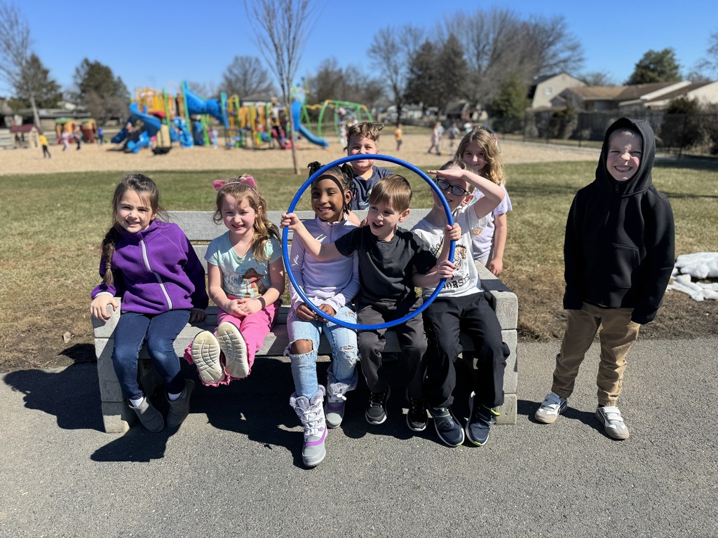 A group of young students sitting on a bench at a playground.