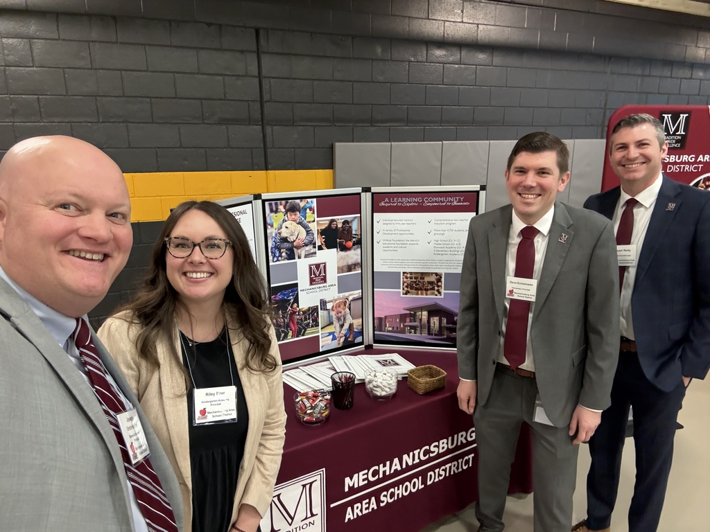 Four principals standing next to a recruitment table at a job fair.