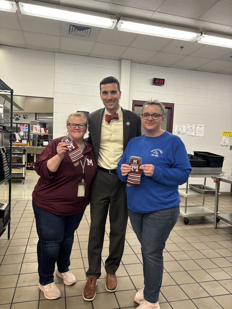 Two food service employees standing in the kitchen next to a man in a suit.