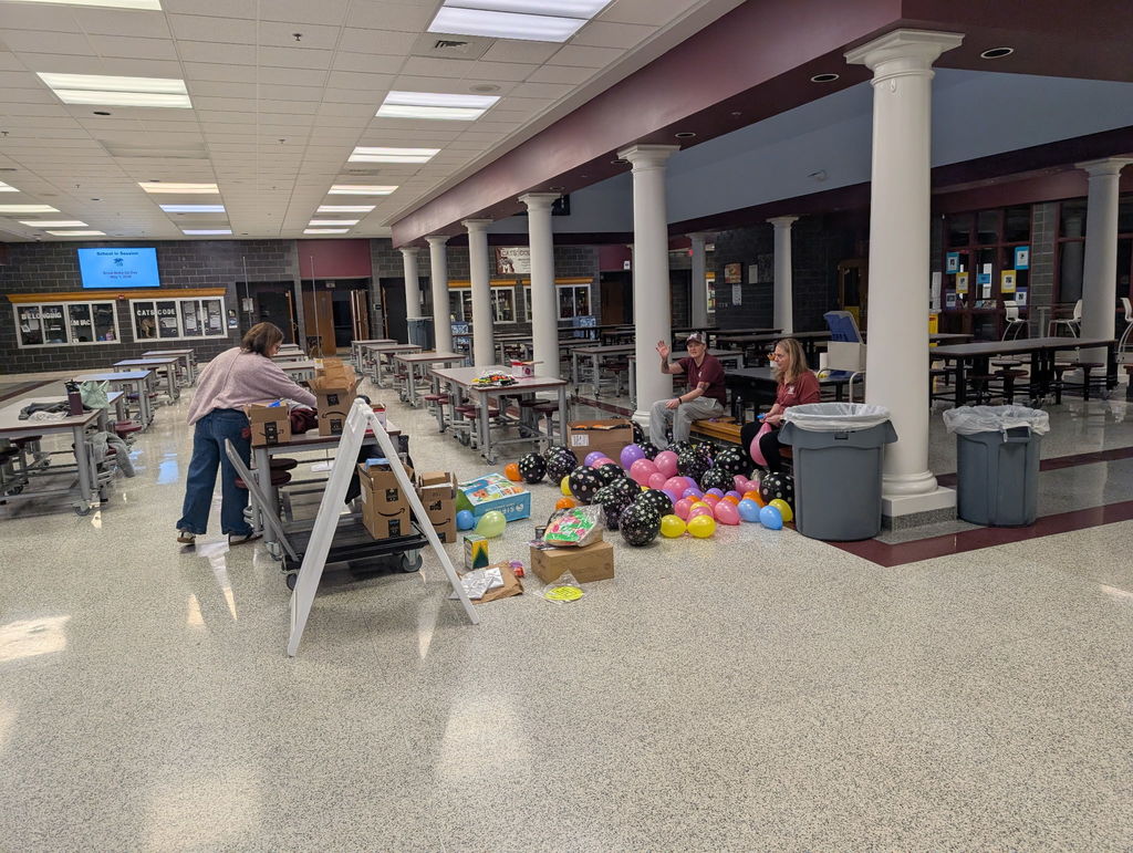 Staff building a balloon arch in a school cafeteria.