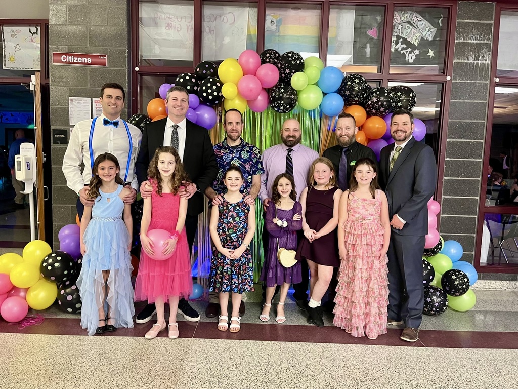 A group of fathers and daughters dressed up and standing in front of a balloon arch.