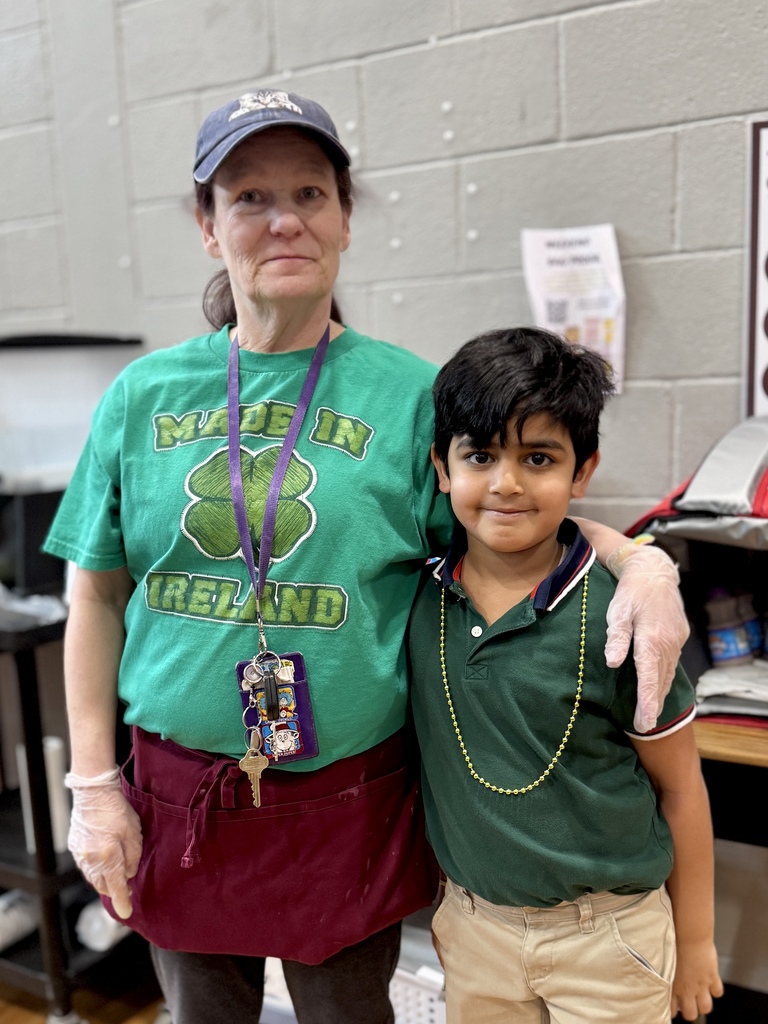 A student and cafeteria working standing side by side in green.