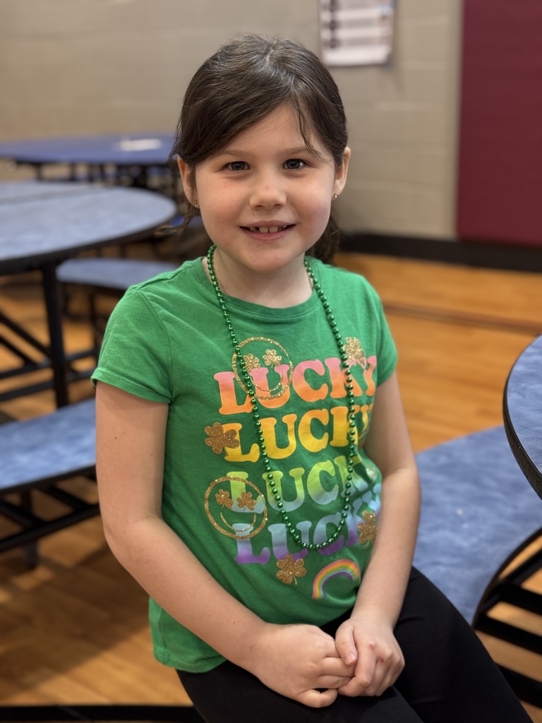 A young student at a table wearing a green shirt and necklace.