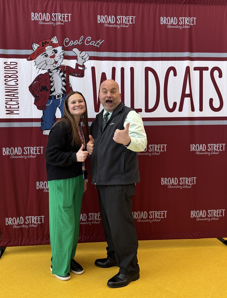 A man and a woman standing in front of a banner and wearing green.
