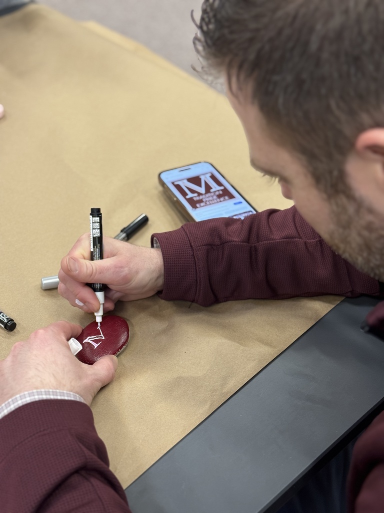 A staff member handpaints a logo on a rock.