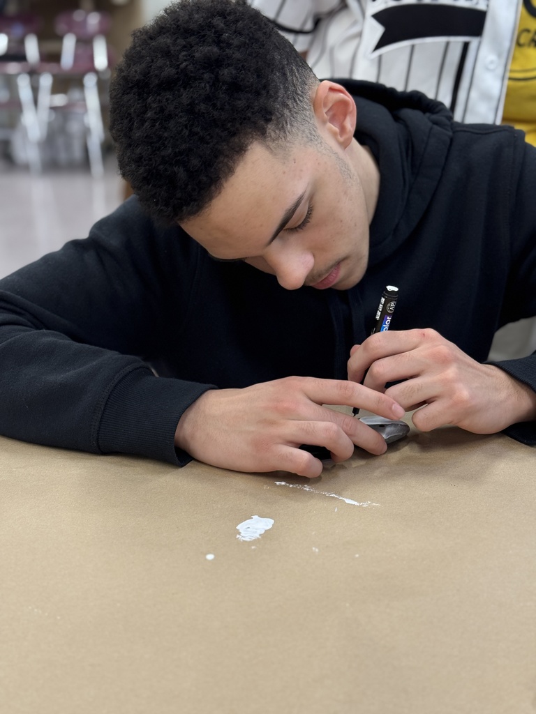 A student hand paints a rock.