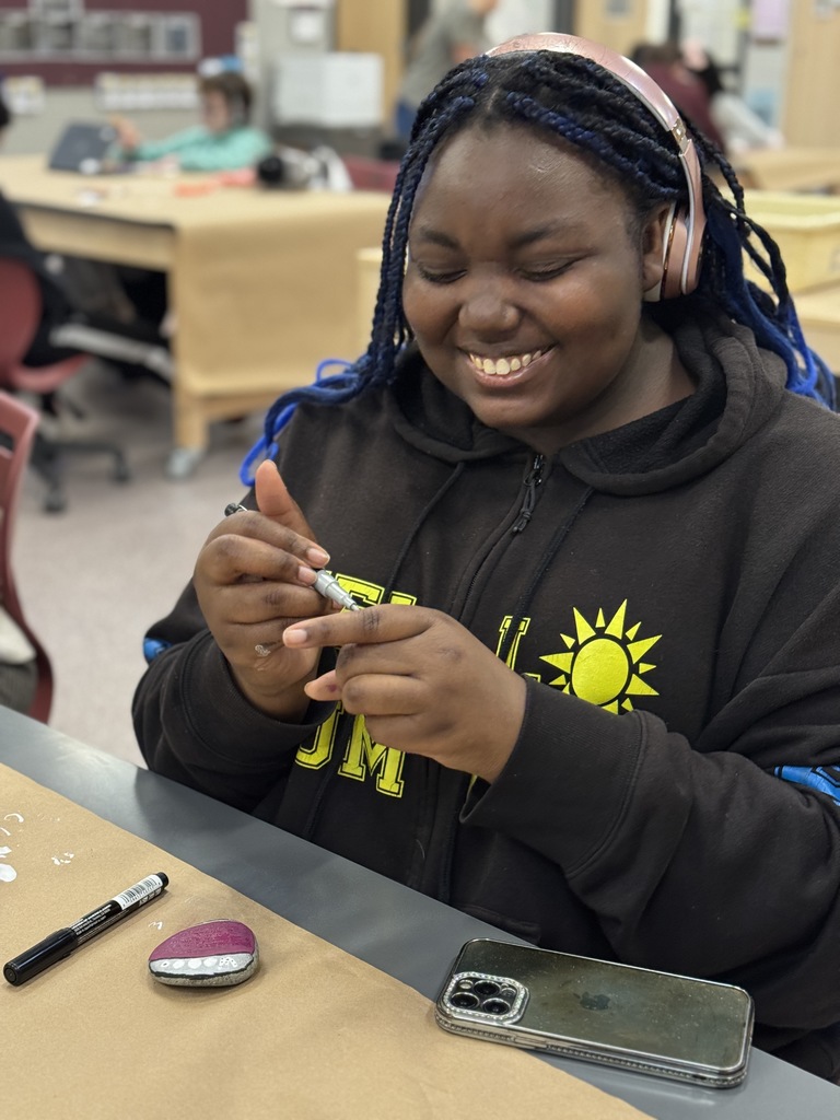 A student is all smiles as she paints a rock.