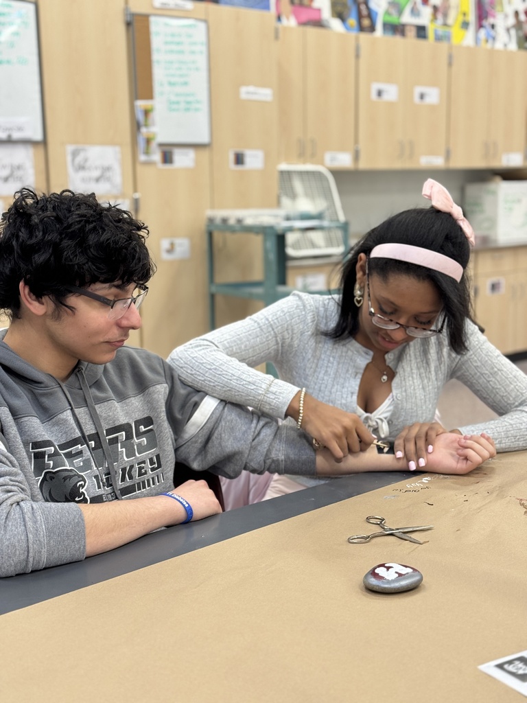 A student paints Henna on a classmates hand.