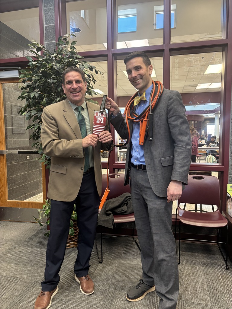A man with jumper cables wrapped around him presents socks to another man.