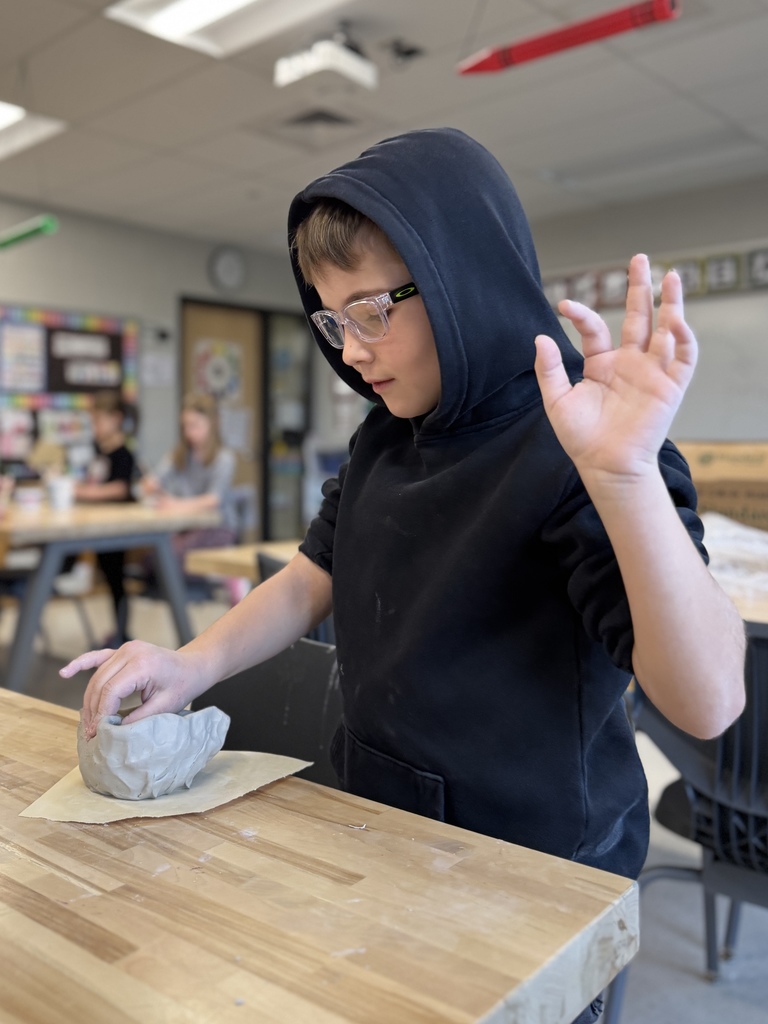 A young boy shapes a clay pot in art class.