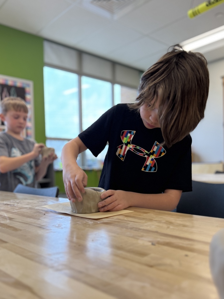 A young boy shapes a clay pot in art class.