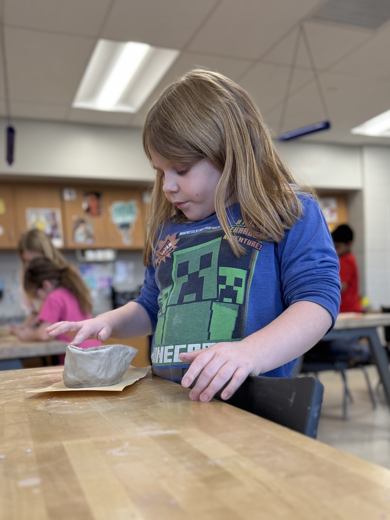 A young girl shapes a clay pot in art class.
