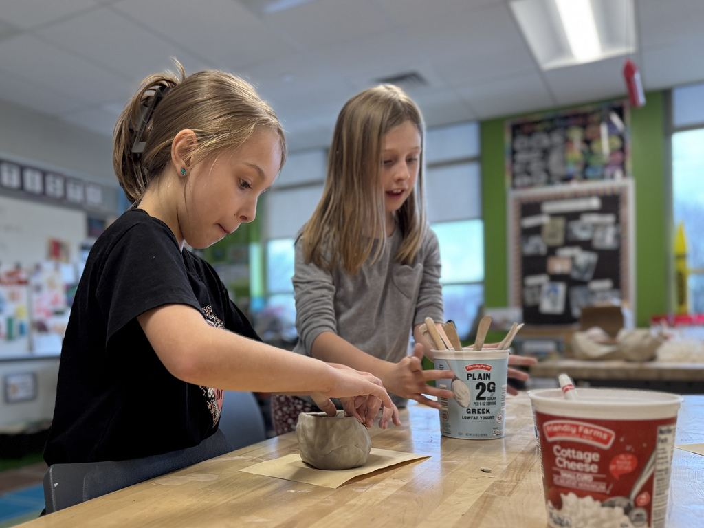 Two young students shape a clay pot in art class.