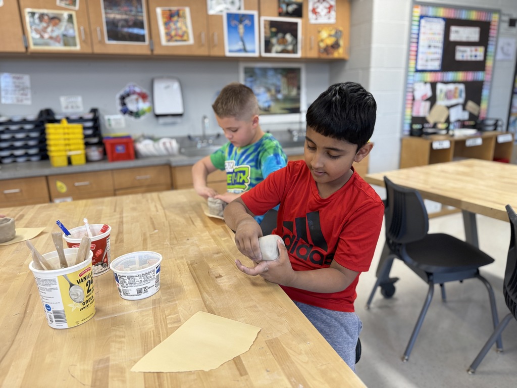 Two young students shape clay pots during art class.