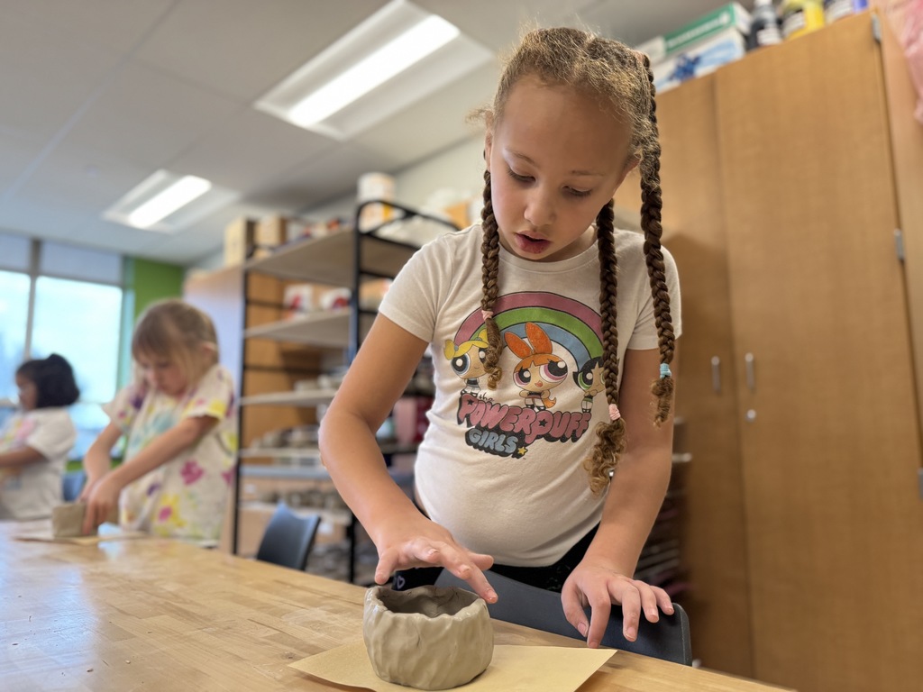 A young girl shapes a clay pot in art class.