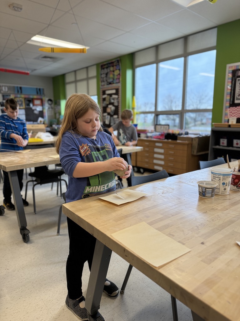 A young girl shapes a clay pot in art class.