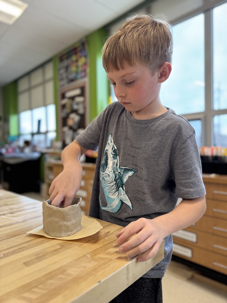 A young boy shapes a clay pot in art class.