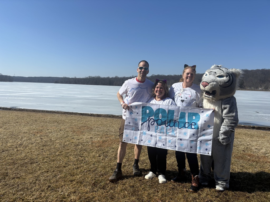 Staff stand in front of a lake that is frozen over.